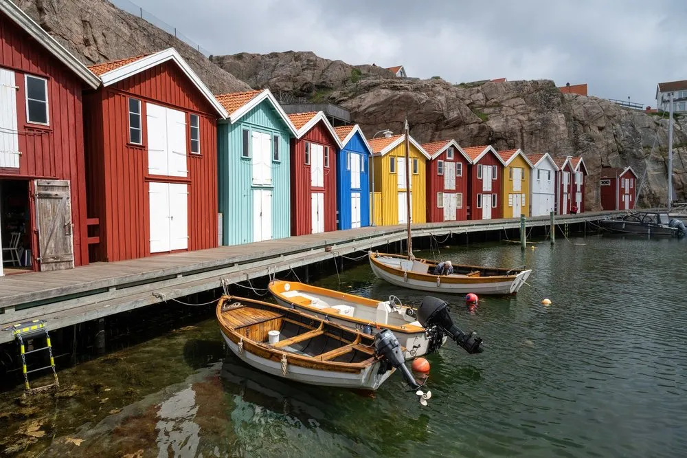 Ein Holzsteg mit roten, blauen und gelben Hütten, davor drei kleine Boote im klaren Wasser