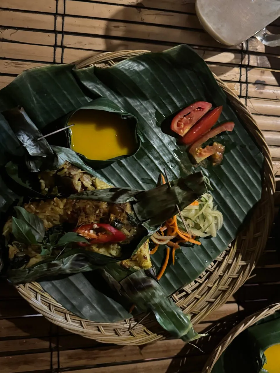 Abendessen auf einem Bananenblatt mit Blattpäckchen, gelber Füllung, Tomatenschnitzen, feinem Salat und einer gelben Sauce