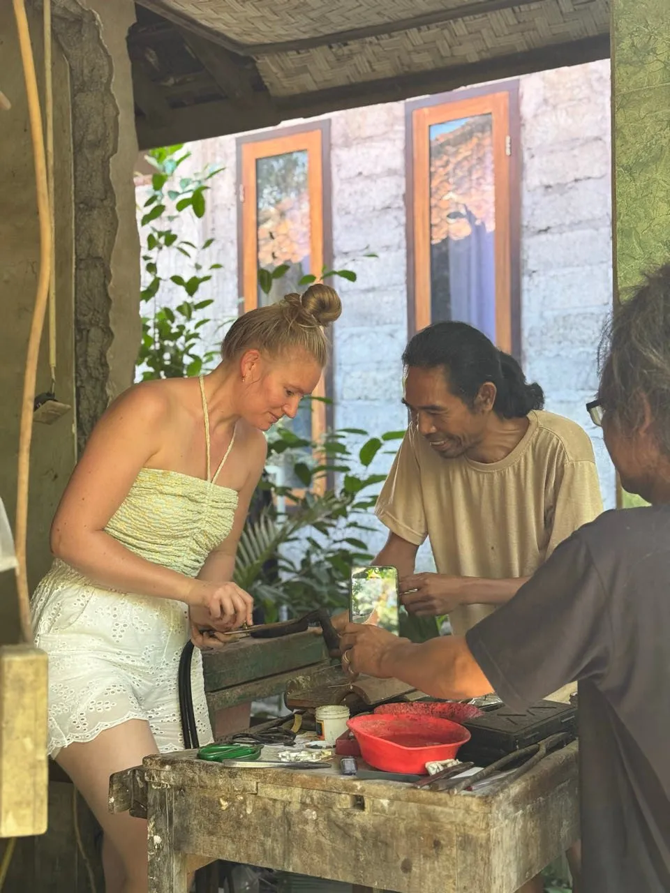 Annina arbeitet in der offenen Werkstatt an einem Holztisch, neben ihr lächelt ein Einheimischer