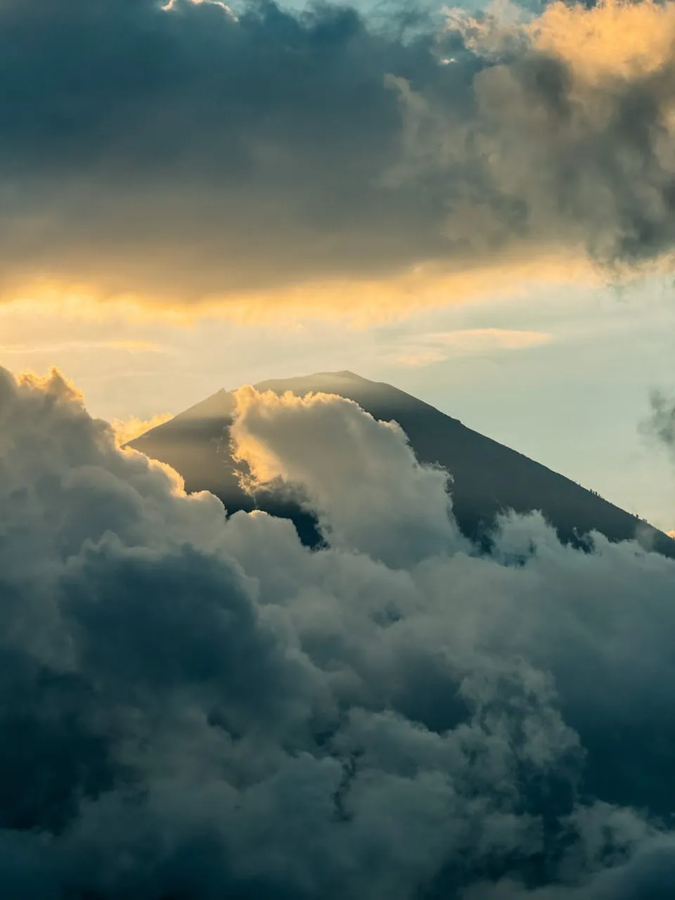 Ein Berggipfel taucht in goldenem Abendlicht zwischen dunklen Wolken auf