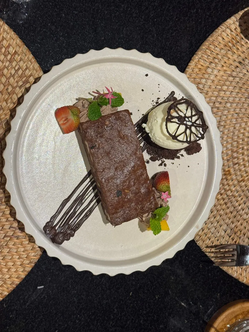 Schokoladenkuchen mit Erdbeeren, Minze, Schokoladengitter und einer Kugel Eis auf einem hellen Teller