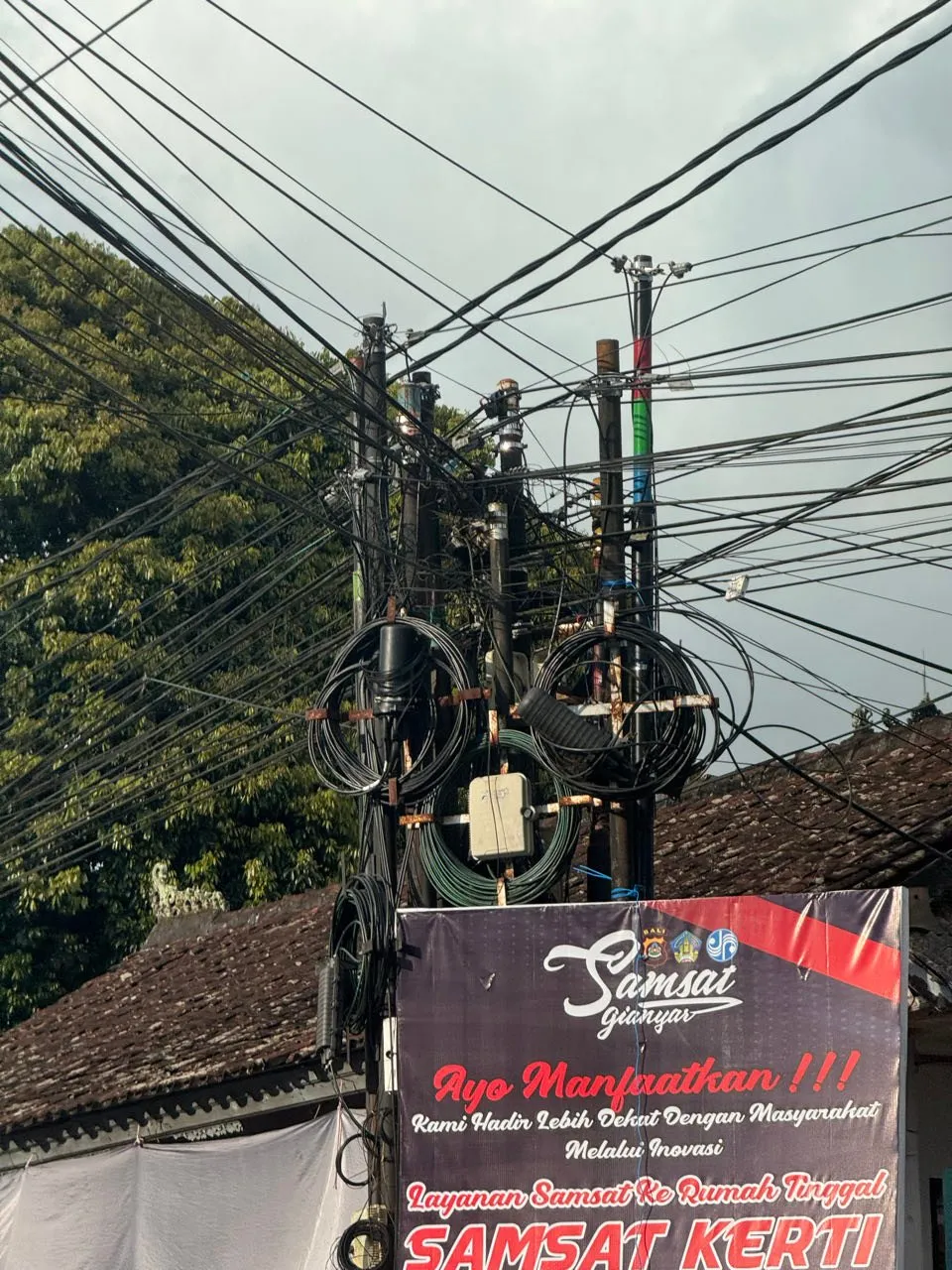 Ein Mast, an dem sehr viele Kabel in alle Richtungen zusammenlaufen, darunter ein Banner mit indonesischer Aufschrift