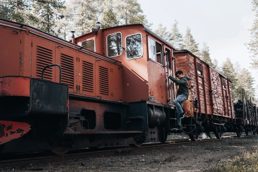 Ein Mann steigt seitlich an der roten Lokomotive hoch, dahinter die Güterwagen und Kiefern