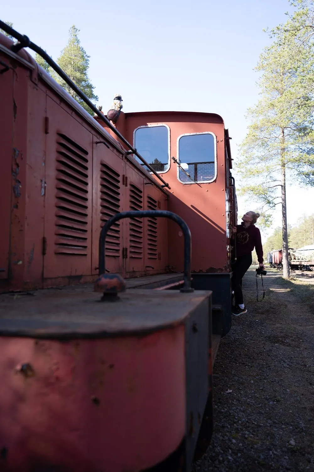 Eine Frau mit Kamera in der Hand blickt an der Seite der Lokomotive nach oben, darüber blauer Himmel