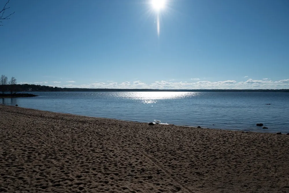 Sandstrand am Wasser, die Sonne spiegelt sich auf dem Meer