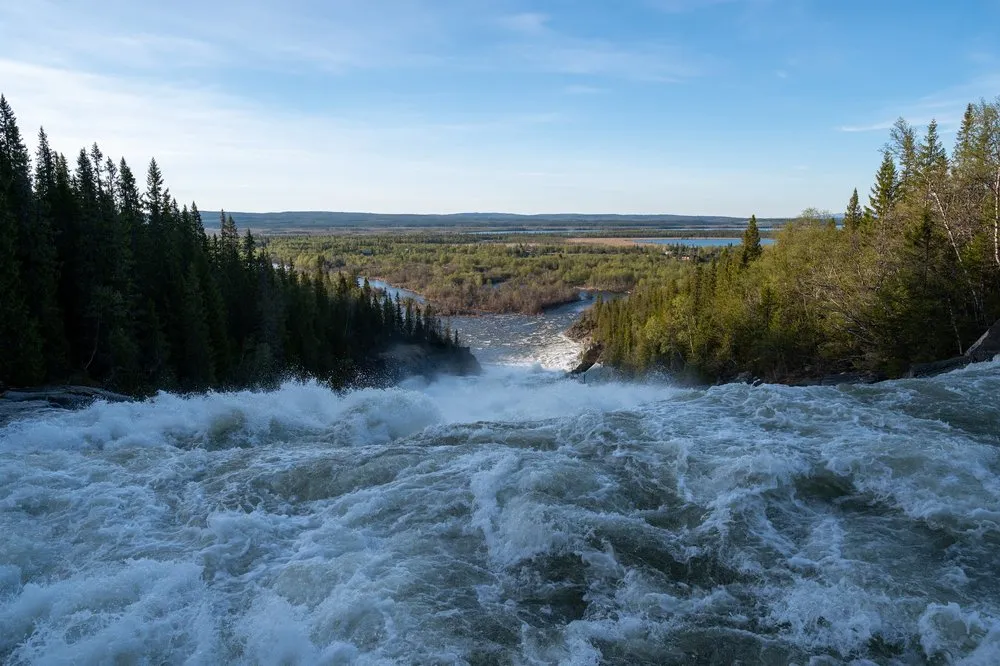 Blick von oben auf die reissenden Stromschnellen des Handölsforsen, dahinter eine weite Landschaft mit Wald und Wasser