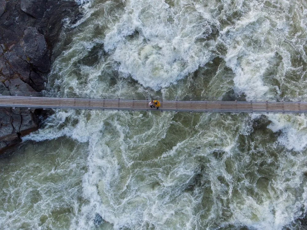 Senkrechte Luftaufnahme der Hängebrücke über dem wirbelnden Wasser des Handölsforsen, in der Mitte zwei kleine Personen
