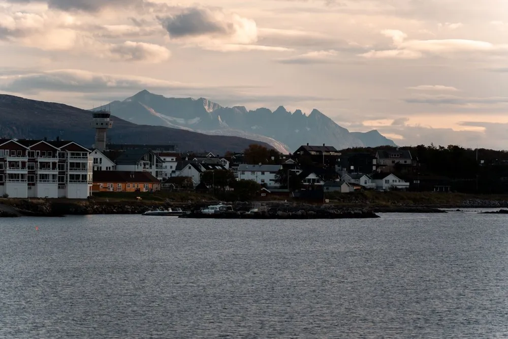 Wohnhäuser und ein Turm am Ufer von Bodø im Licht des späten Nachmittags, dahinter eine gezackte Bergkette