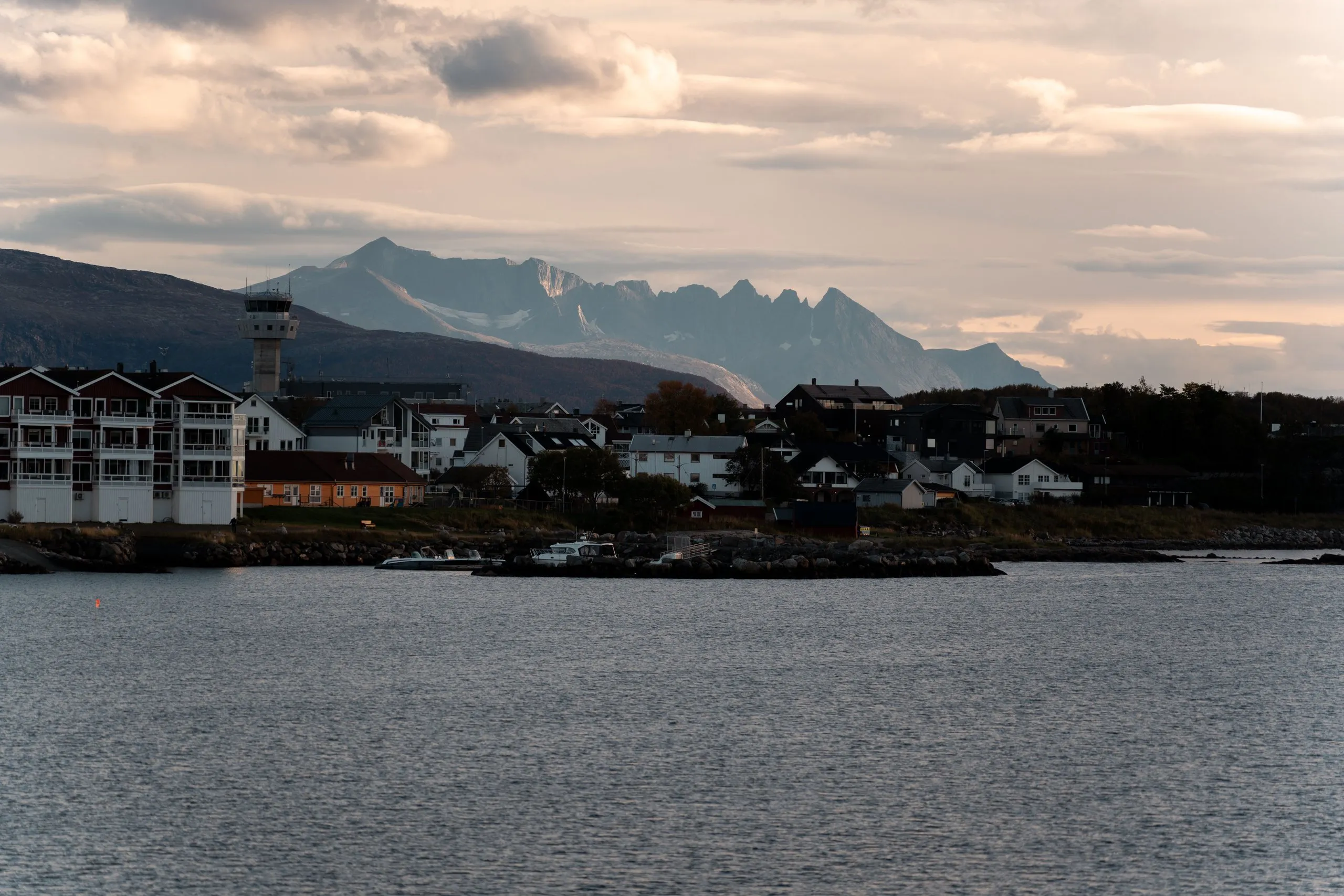 Wohnhäuser und ein Turm am Ufer von Bodø im Licht des späten Nachmittags, dahinter eine gezackte Bergkette