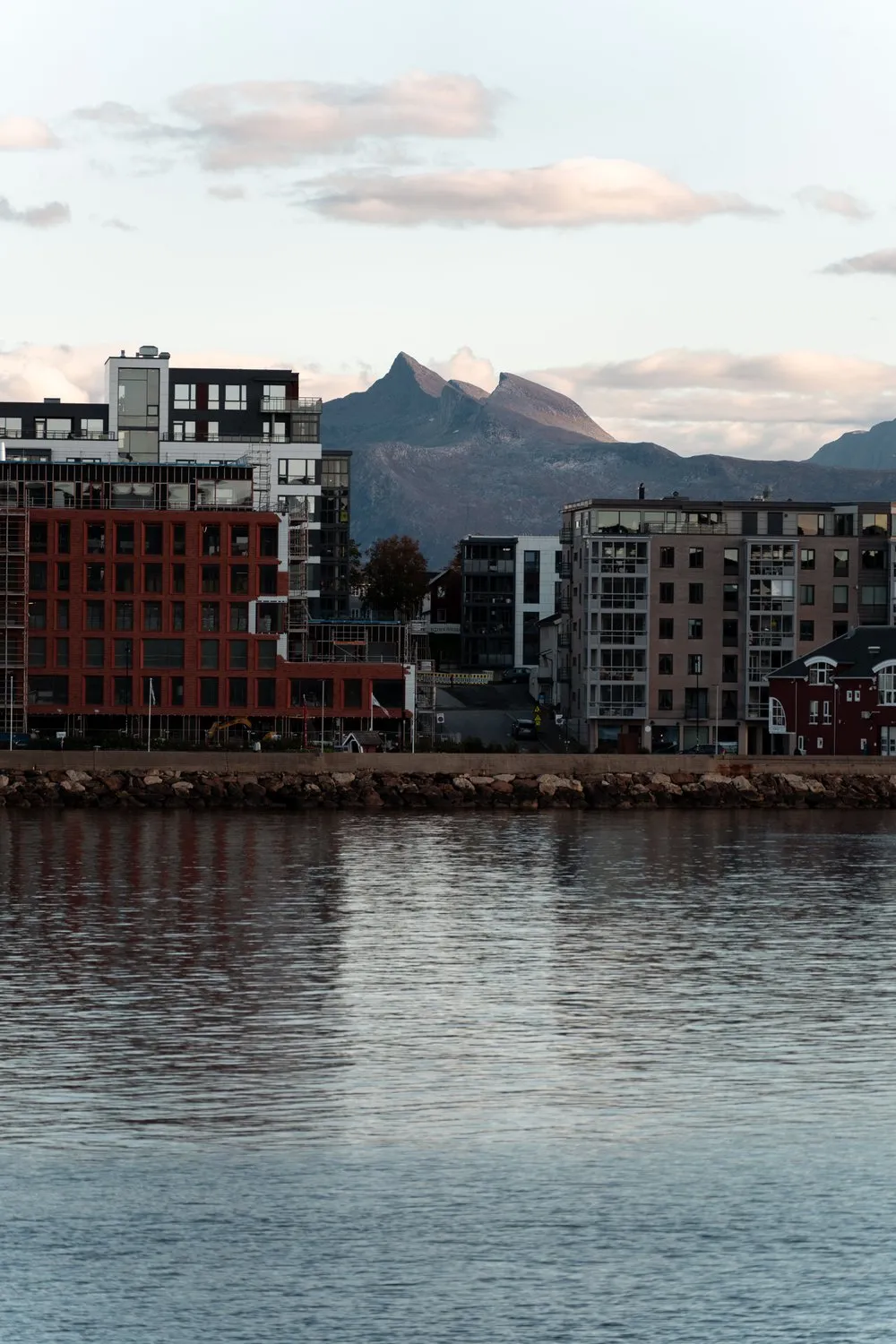Moderne Wohnhäuser am Ufer von Bodø, an einem roten Backsteinbau steht noch das Gerüst, dahinter ein Berg mit zwei Spitzen