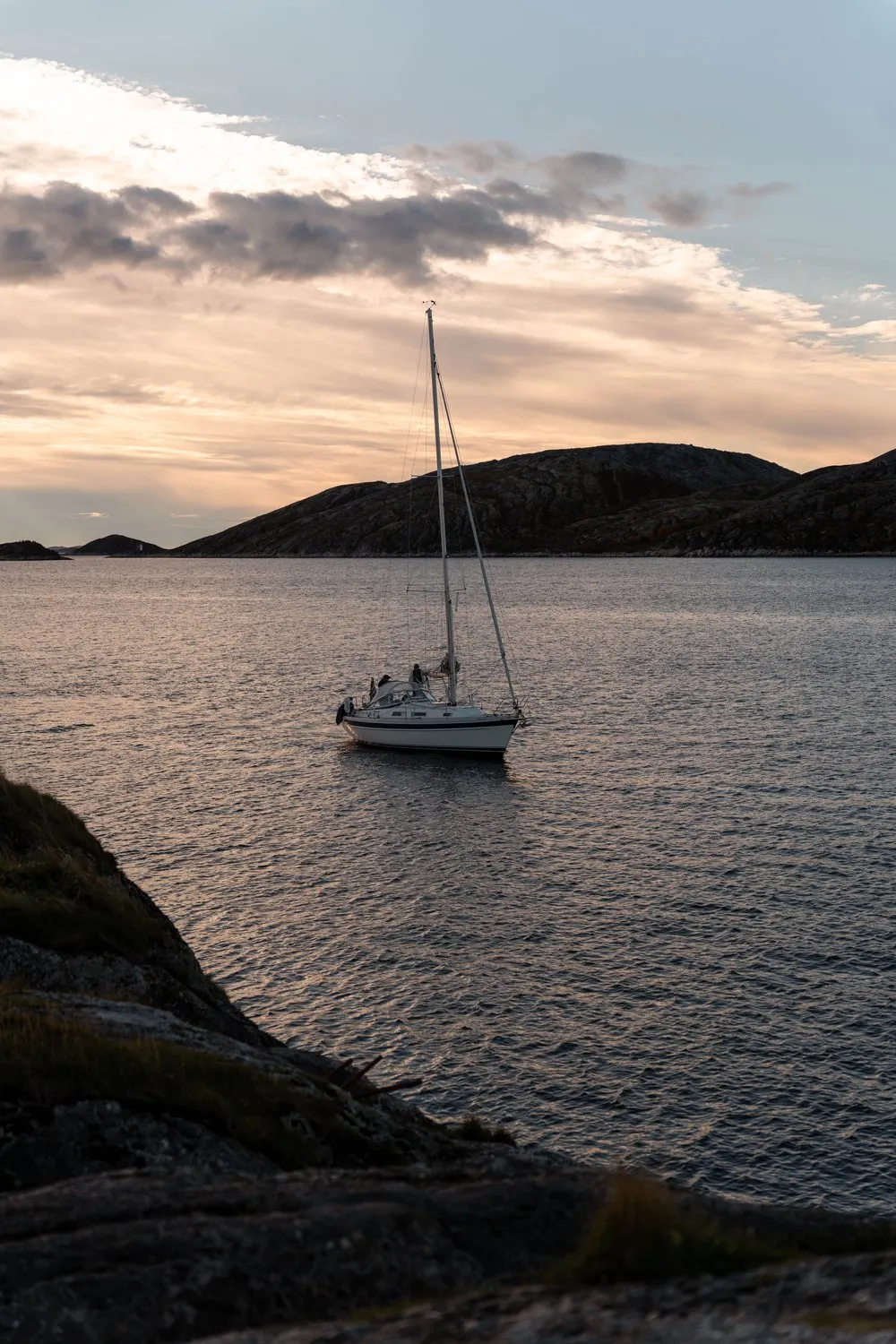 Ein Segelboot vor der felsigen Küste bei Bodø, im Vordergrund die Felsen am Ufer