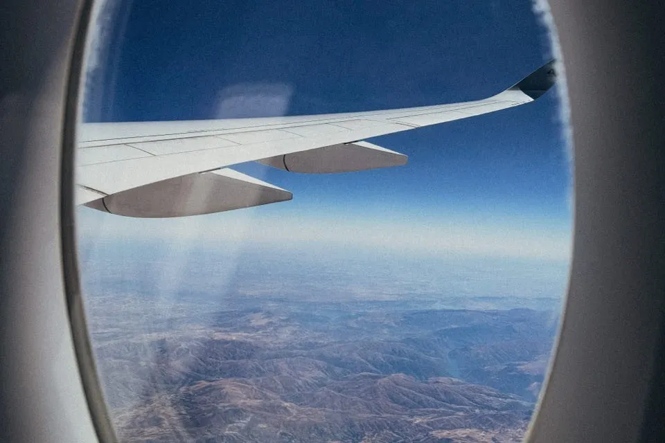 Flugzeugflügel vor tiefblauem Himmel über braunen, zerfurchten Bergen