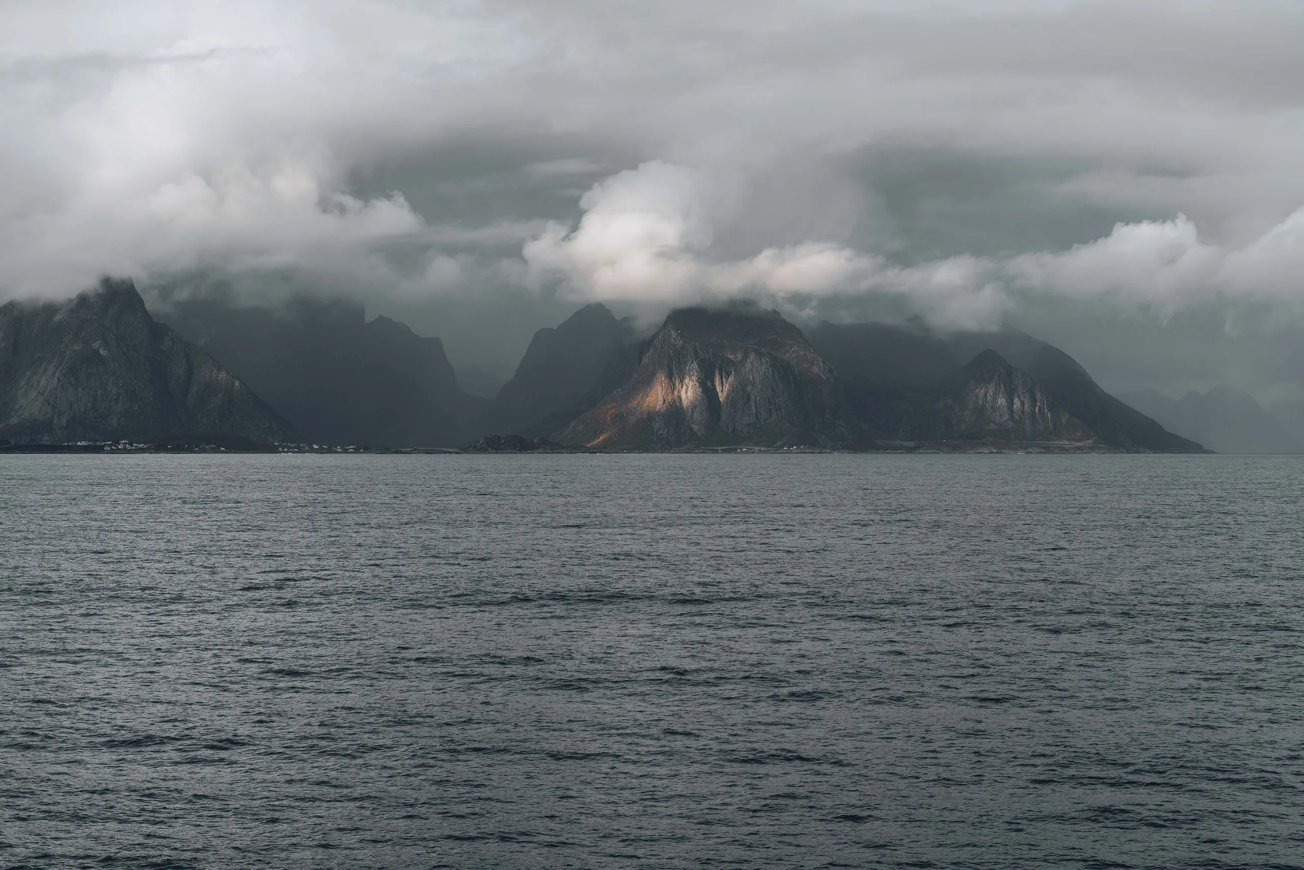 Die Berge der Lofoten unter tiefen Wolken, von der Fähre aus gesehen, ein Gipfel liegt im Licht