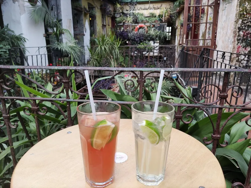 Zwei Cocktails mit Limettenscheiben auf einem runden Tisch, dahinter der begrünte Innenhof der Ruinenbar