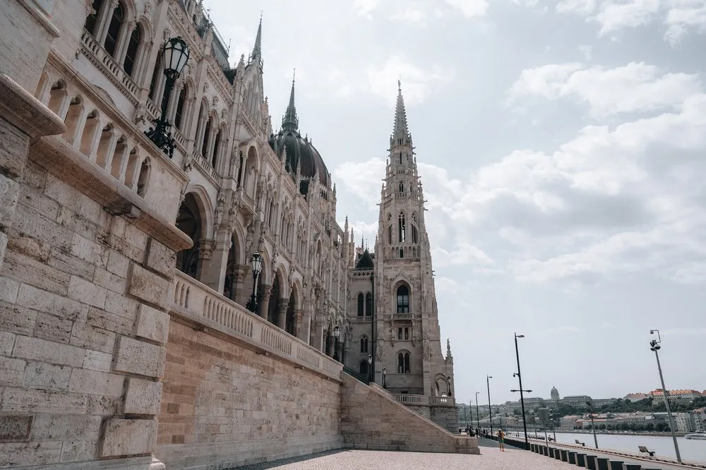Das Parlamentsgebäude von der Seite, links die Steinmauer, rechts die Uferpromenade an der Donau