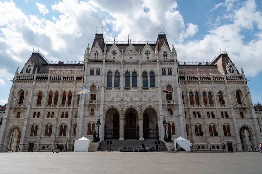 Die Fassade des Parlamentsgebäudes mit drei Portalbögen und einer Treppe, davor ein weiter Platz mit zwei kleinen Zelten
