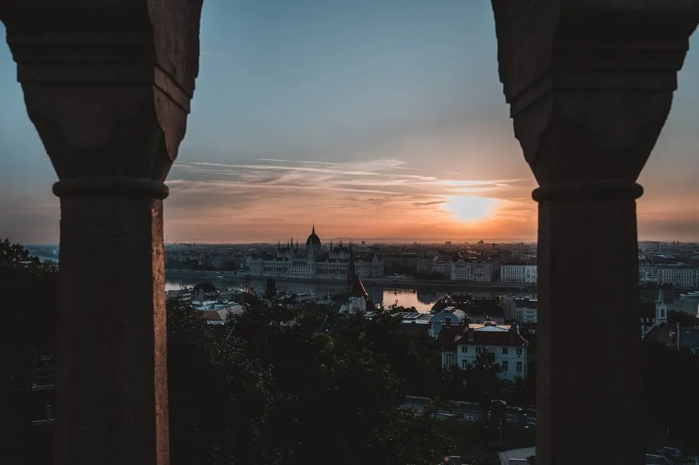 Die aufgehende Sonne zwischen zwei Säulen, unten die Stadt mit dem Parlament am Fluss