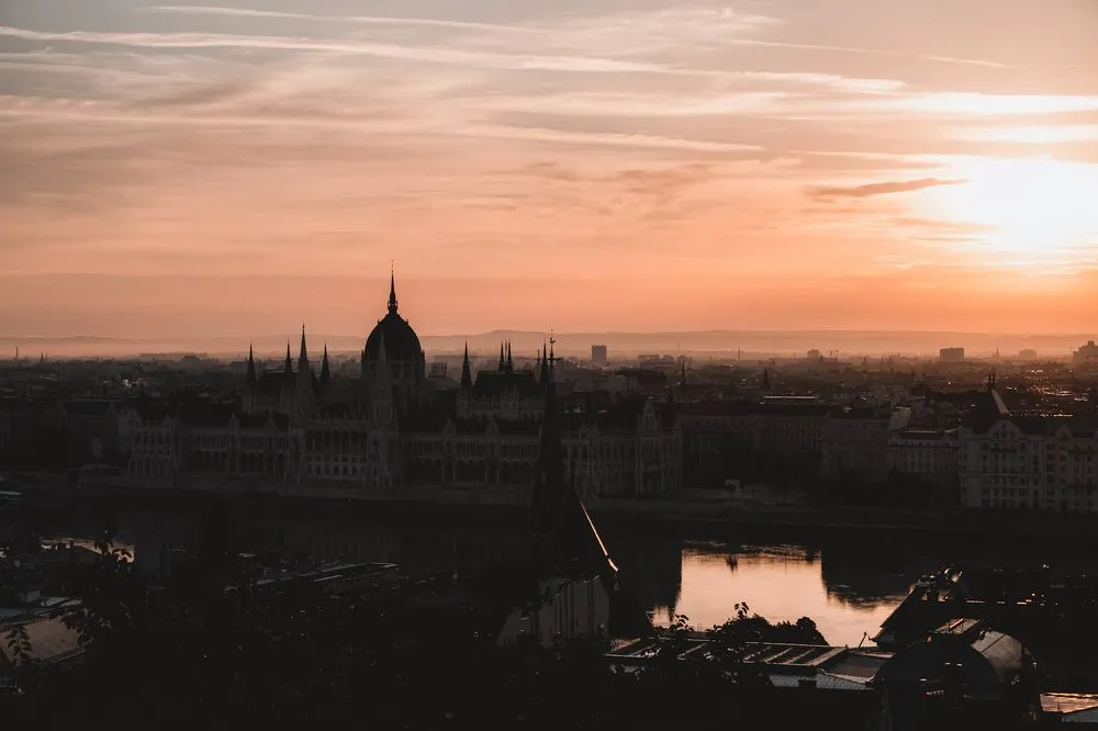 Das Parlament im orangeroten Morgenlicht, näher herangezoomt, rechts oben die Sonne über der Stadt