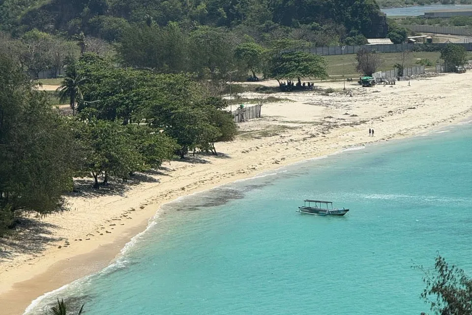 Ein kleines Boot liegt in türkisfarbenem Wasser vor einem hellen Sandstrand mit Bäumen