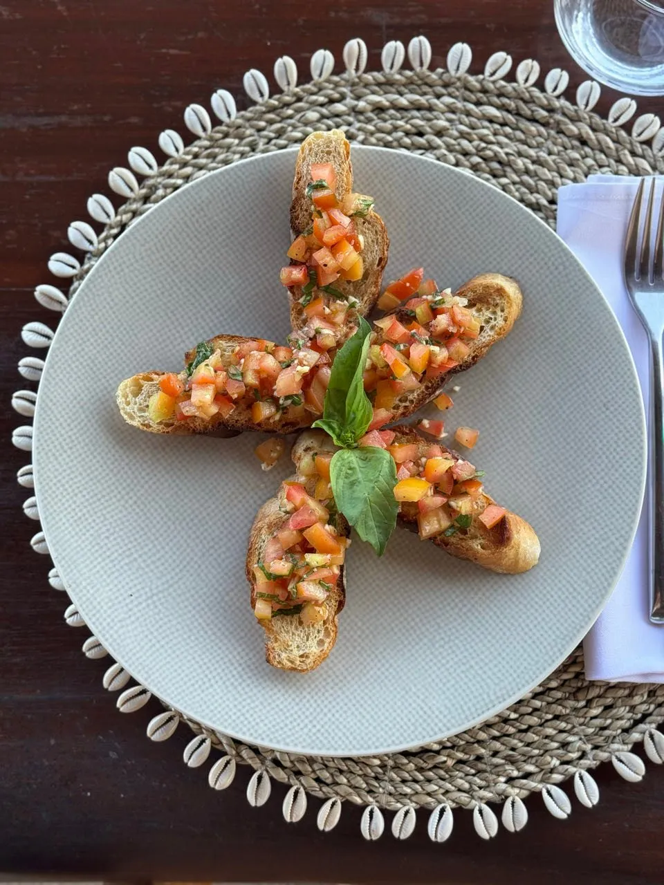 Fünf Bruschetta mit gehackten Tomaten und einem Basilikumblatt, sternförmig auf einem hellen Teller angerichtet