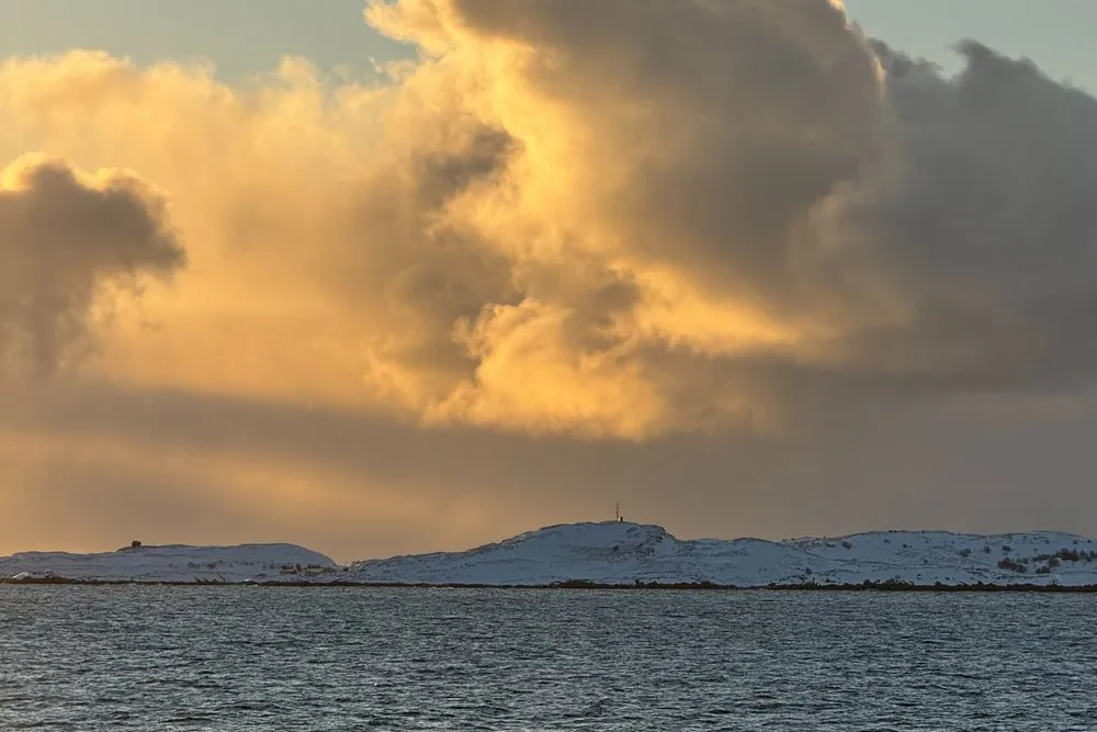 Eine goldbeleuchtete Wolkenwand über dem Meer, von der Fähre aus gesehen