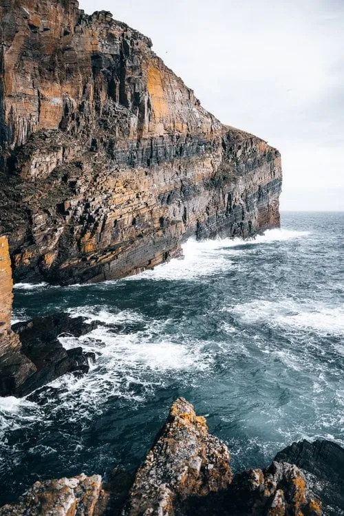 Tilted sandstone cliffs at the Whaligoe Steps, surf breaking below