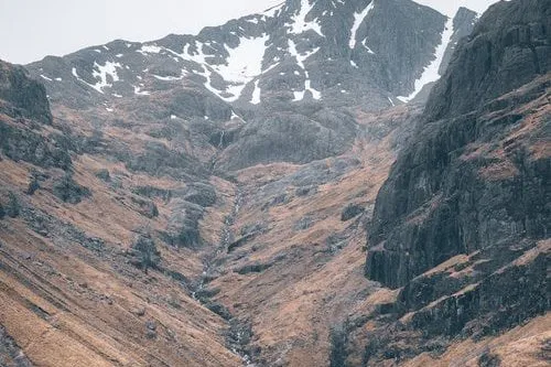 Eine schmale Schlucht im Glen Etive, dahinter ein schneegefleckter Gipfel