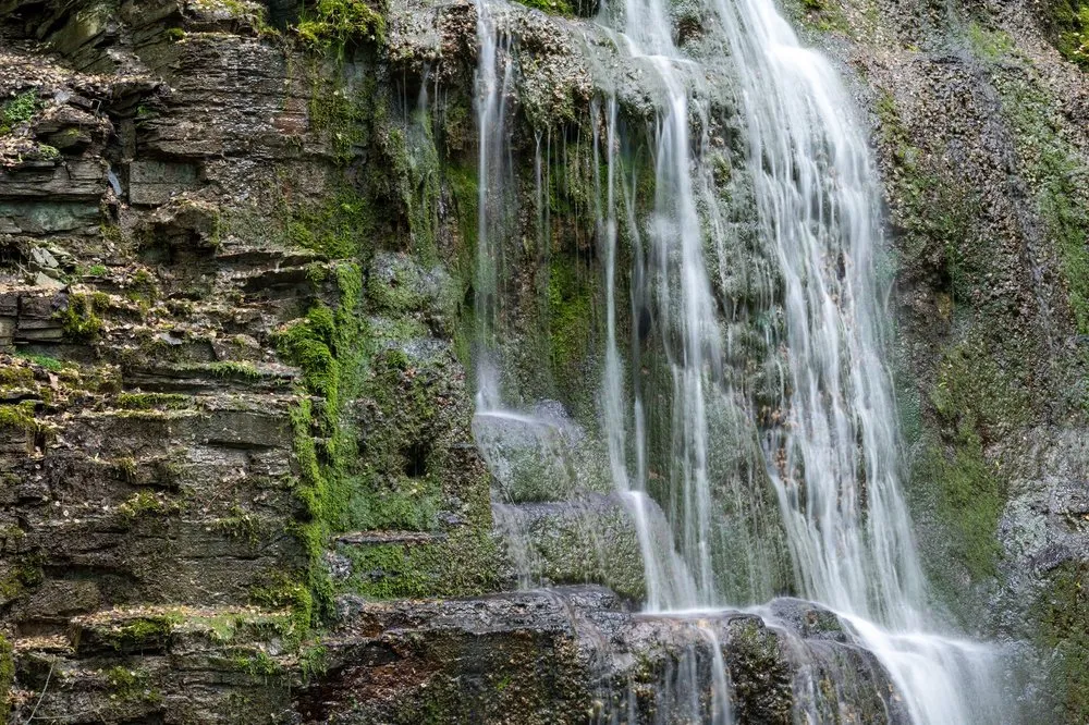 Nahaufnahme von feinen Wasserschleiern über Felsstufen mit Moos