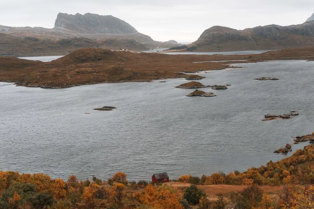 Ein See mit kleinen Inseln zwischen den Bergen, am Ufer ein rotes Haus im orangen Herbstlaub