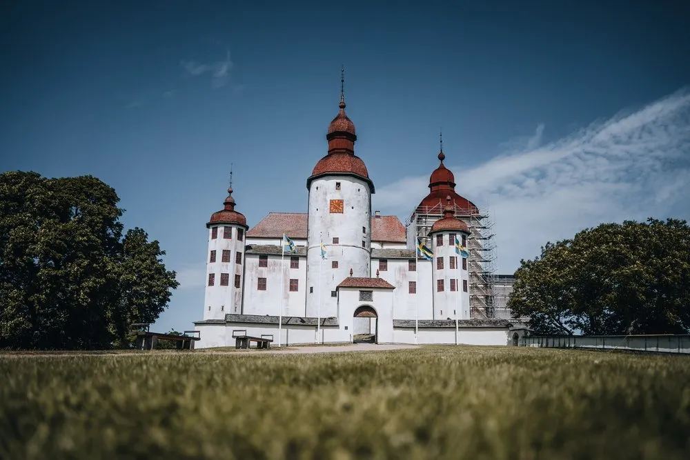 Läckö Slott mit roten Turmhauben von einer Wiese aus, an einem Turm steht ein Baugerüst