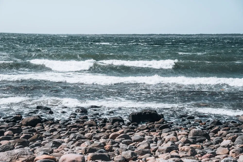 Waves with white crests roll onto a beach of round stones
