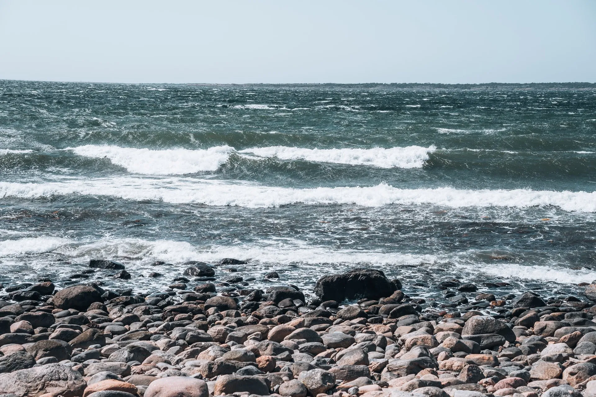 Wellen mit weissen Schaumkronen rollen auf einen Strand aus runden Steinen