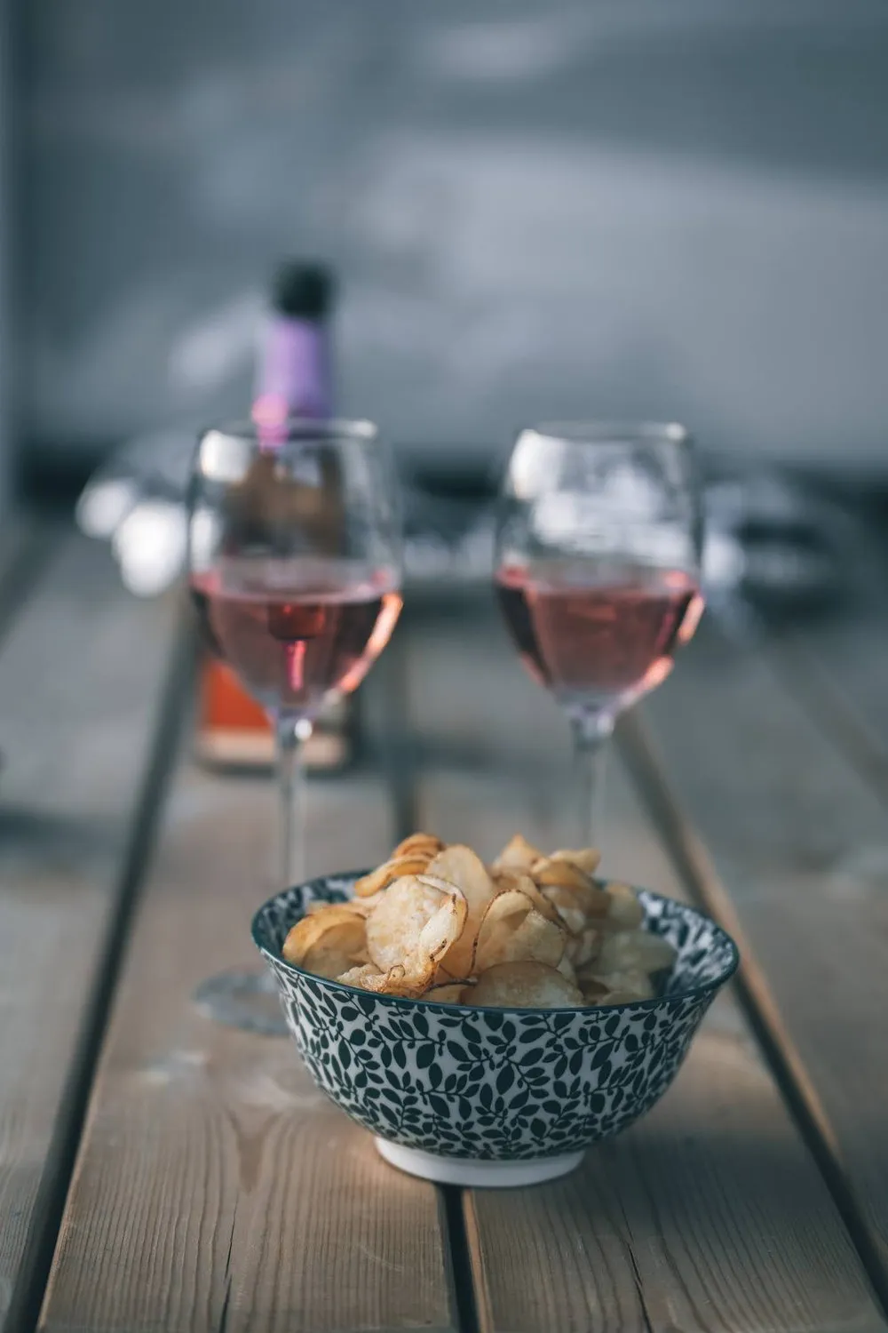 Zwei Gläser Rosé und eine Schale Chips auf einem Holztisch