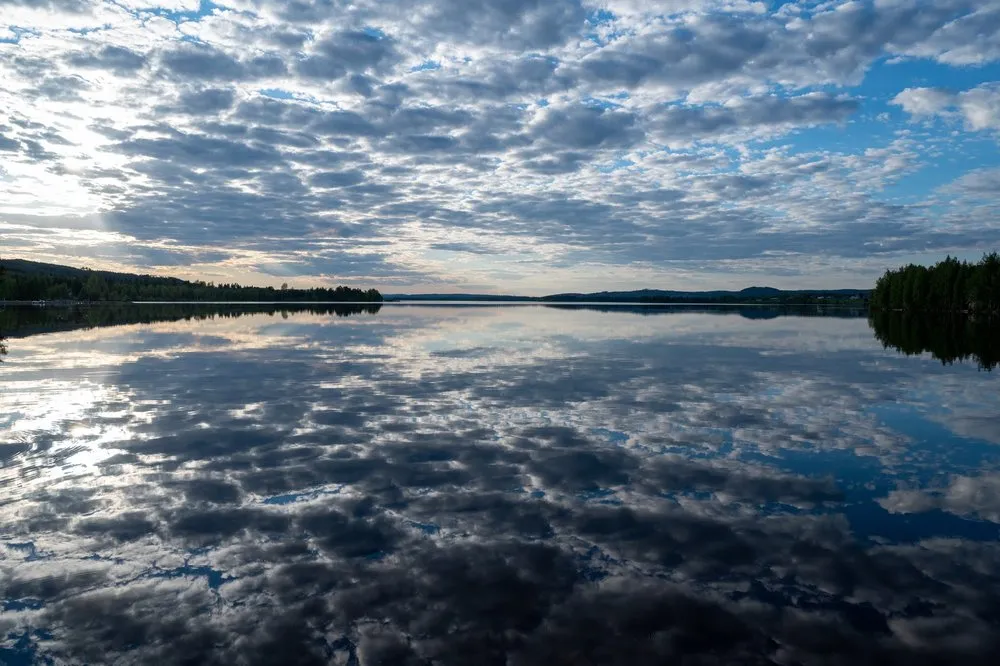 Wolken spiegeln sich in einem ruhigen See, links und rechts bewaldete Ufer