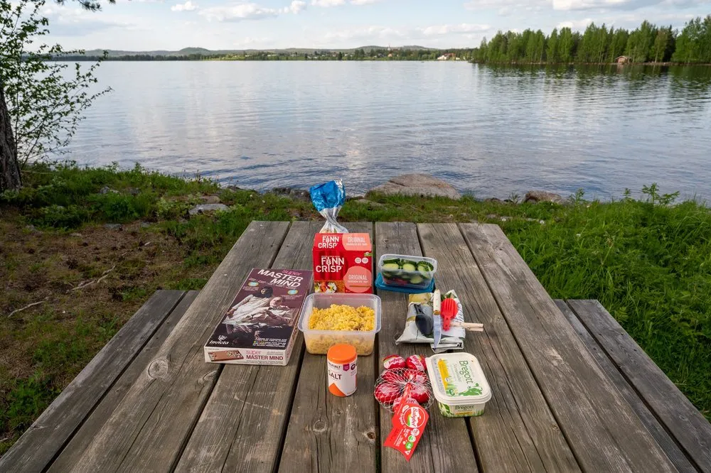 Picknicktisch am Seeufer bei Rätan mit Curryreis, Knäckebrot, Butter und einer Spielschachtel