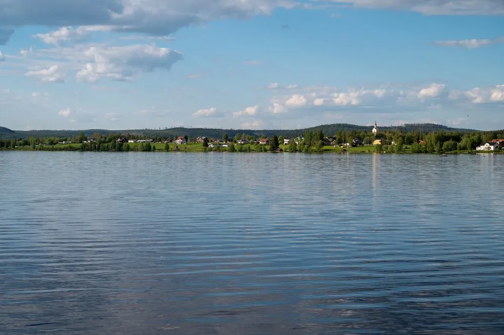 Blick über den See auf ein Dorf mit hellem Kirchturm am gegenüberliegenden Ufer