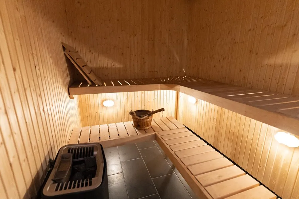 Die Sauna in der Wohnung mit hellen Holzbänken, einem Holzeimer mit Schöpfkelle und dem elektrischen Ofen