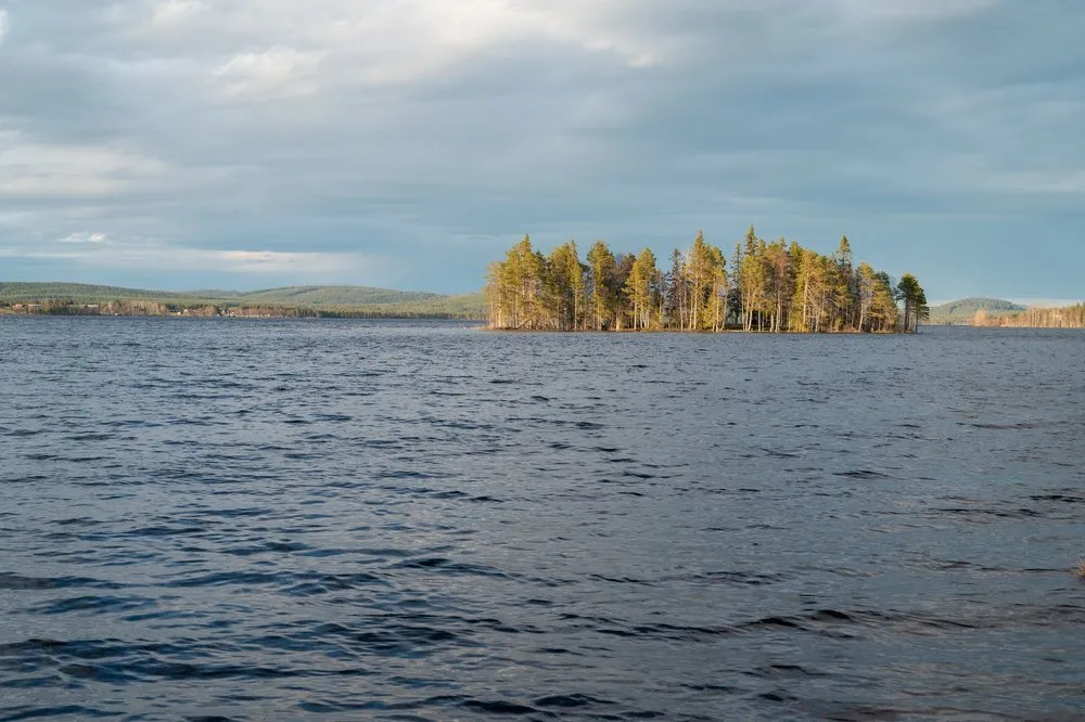 Eine kleine bewaldete Insel im warmen Abendlicht, davor der leicht gekräuselte See