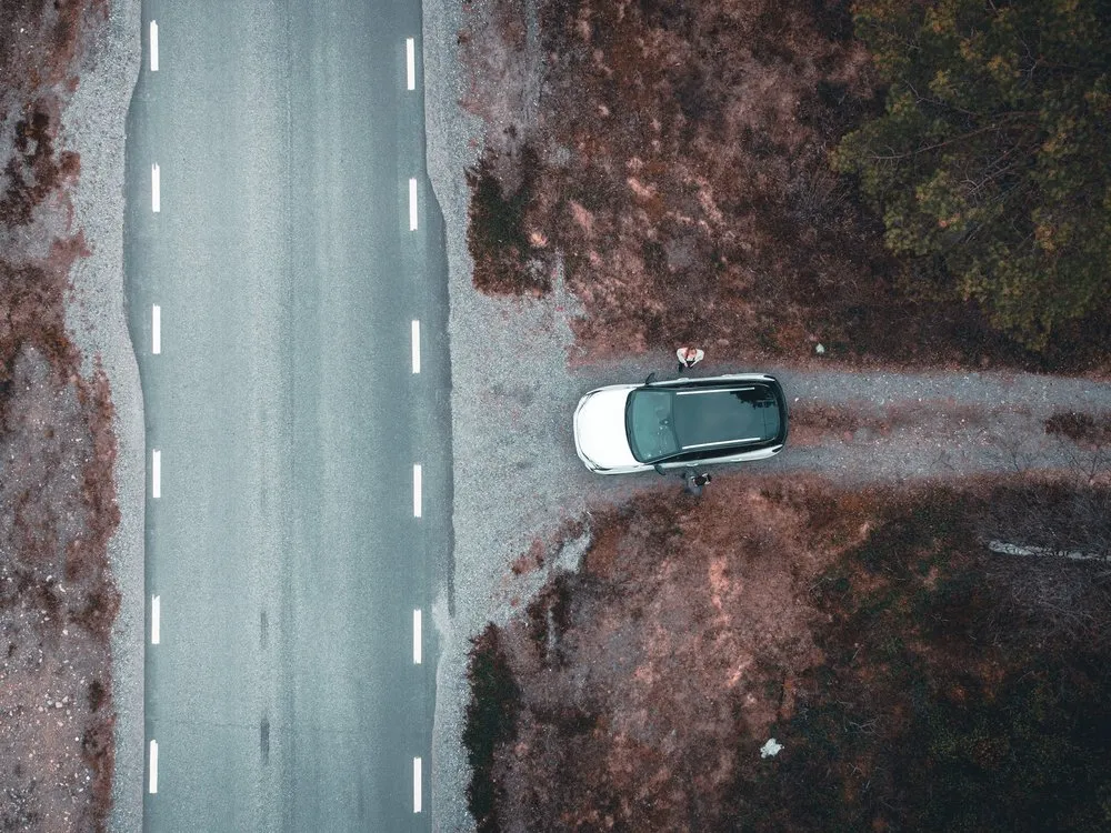 Drohnenblick auf ein weisses Auto in einer Kiesbucht neben der Strasse