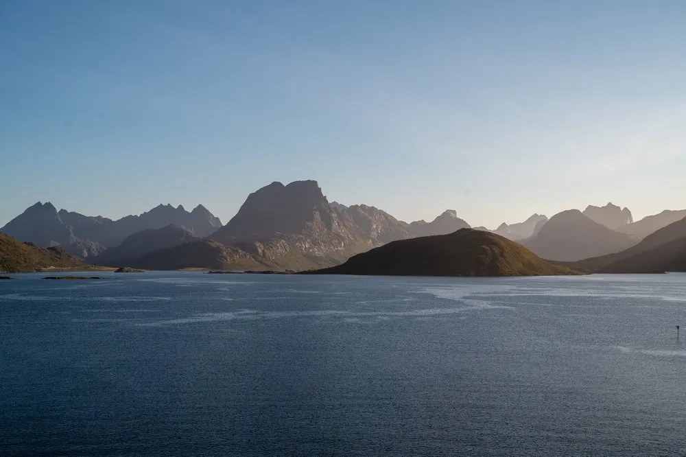 Gestaffelte Bergketten im Abendlicht über dem Wasser, davor eine dunkle Insel