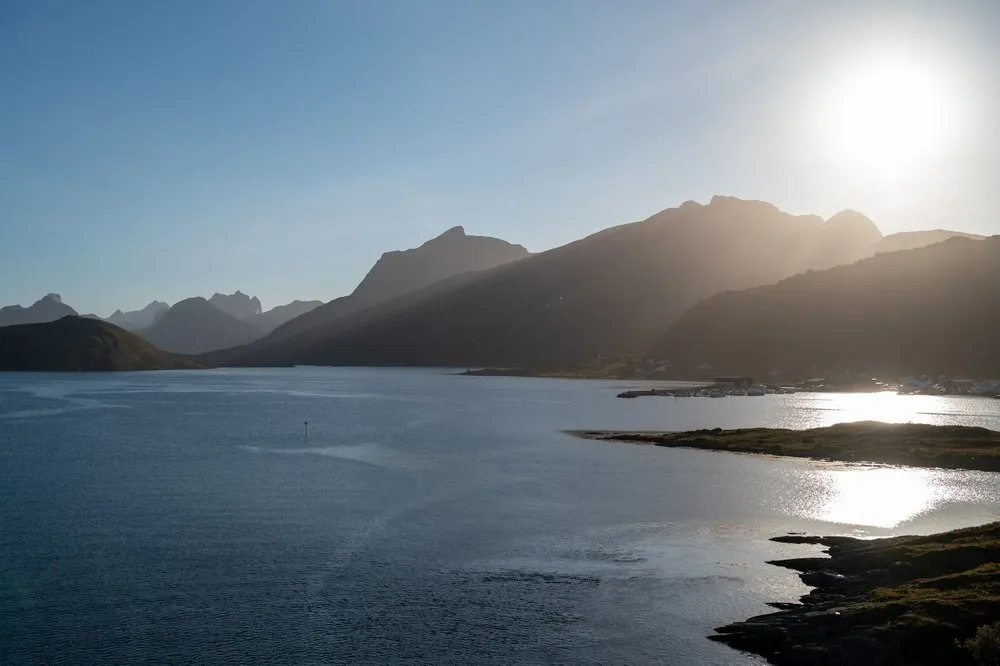 Die tief stehende Sonne über den Bergen, im Wasser spiegelt sich das Licht, am Ufer stehen Häuser