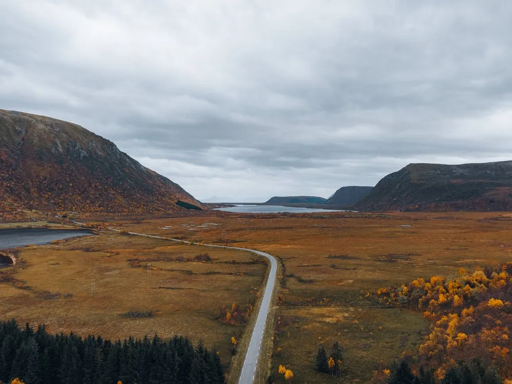 Eine Strasse durch eine weite, herbstlich braune Ebene zwischen zwei Bergen, aus der Luft auf dem Rückweg nach Nøss
