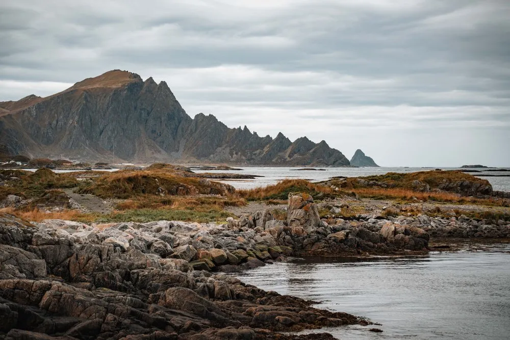 Felsen und Wasser beim Leuchtturm von Andenes, dahinter die gezackten Berge von Andøya