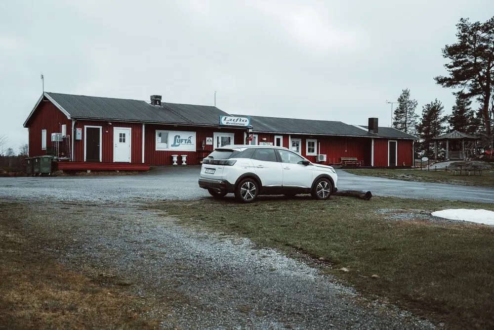 Das rote Haus des Campingplatzes Lufta mit Schild, davor ein weisses Auto auf dem Kiesplatz