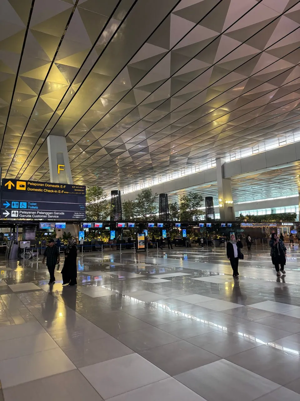 Hohe Halle mit Decke aus dreieckigen Paneelen, Schilder «Domestic Check-in E-F» und «Garuda Customer Service», einzelne Reisende