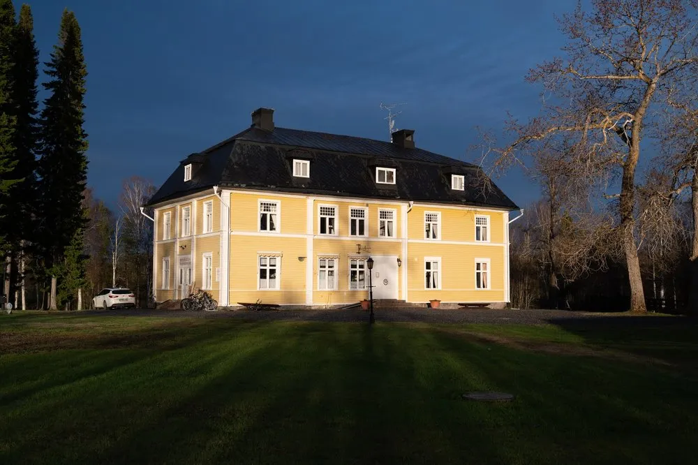 Die gelbe Villa Melderstein Herrgård mit dunklem Dach im letzten Sonnenlicht vor einem dunkelblauen Himmel