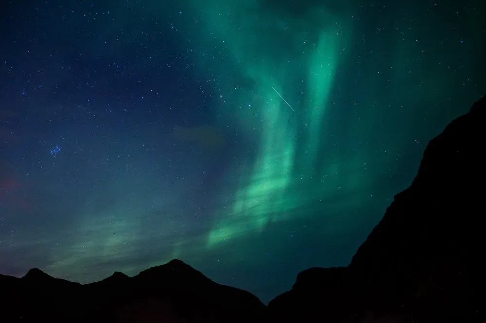 Grünes Nordlicht steigt hinter schwarzen Bergsilhouetten in den Sternenhimmel
