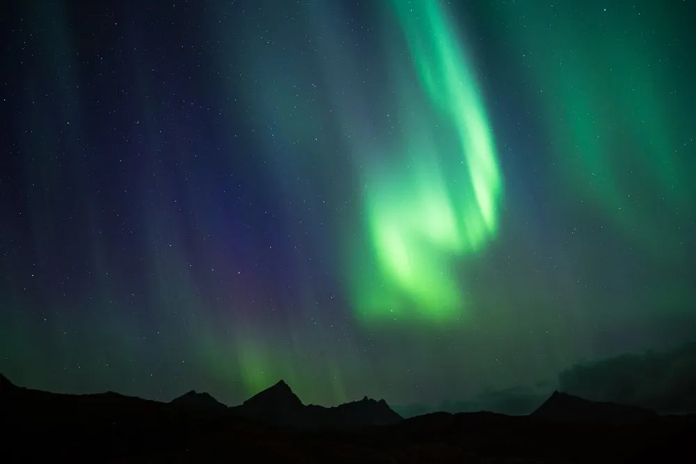Ein Nordlicht mit grünen und violetten Strahlen über den Spitzen dunkler Berge
