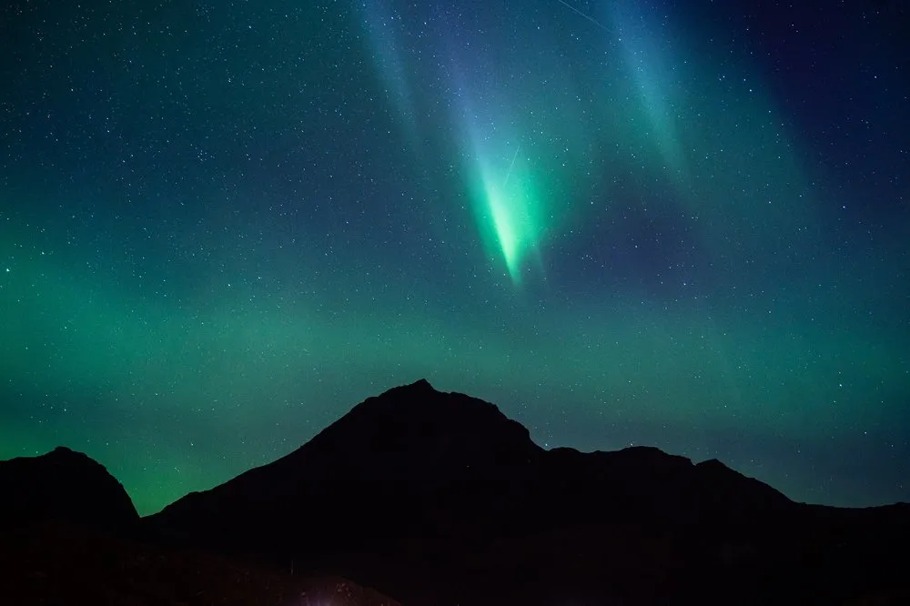 Ein heller grüner Strahl über einer dunklen Bergspitze