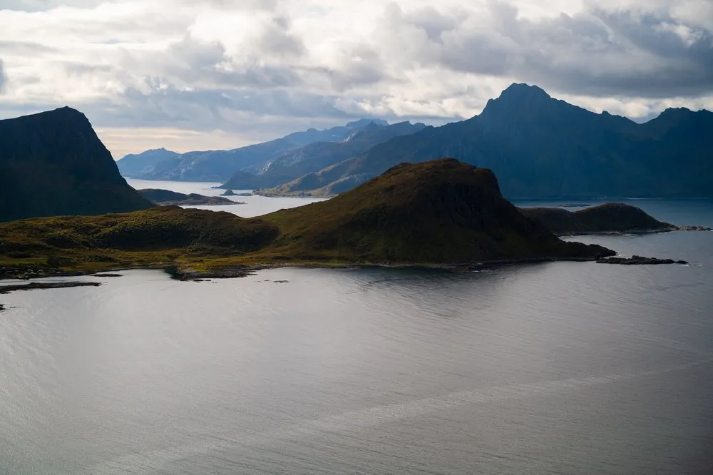 Eine grüne Halbinsel und dahinter gestaffelte Berge über dem ruhigen Meer